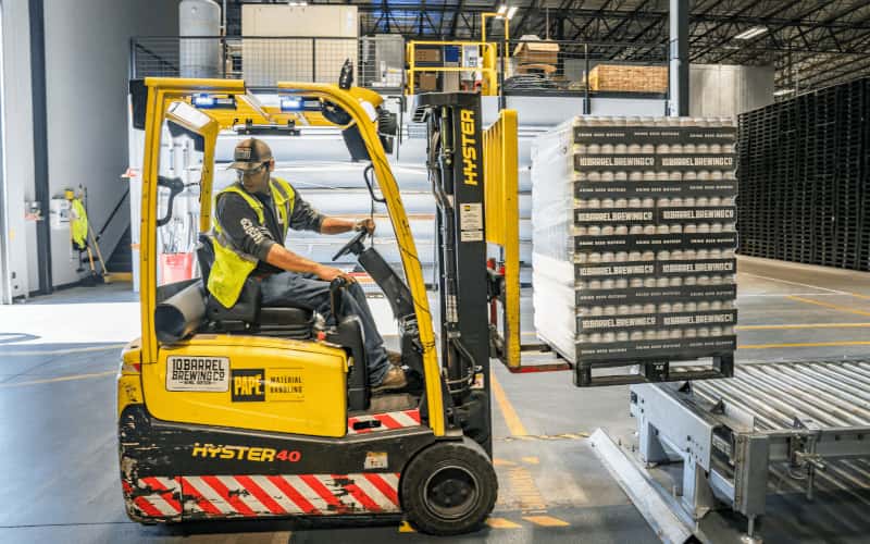 man operating forklift picking up pallet in warehouse storage