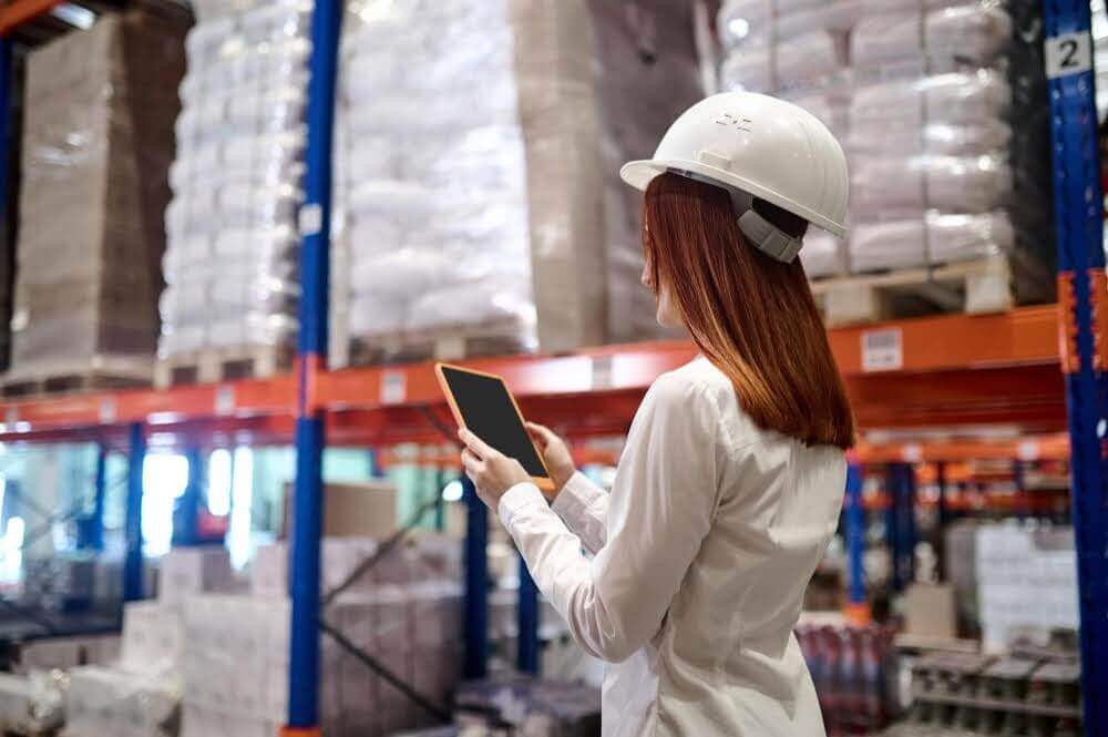 Warehouse supervisor utilizing a digital tablet to oversee high-volume inventory, exemplifying how technology acts as the brain behind the brawn in modern logistics operations.